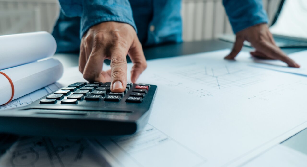 A person using a calculator over building plans, representing EWI Store – a company specialising in external wall insulation and render systems.