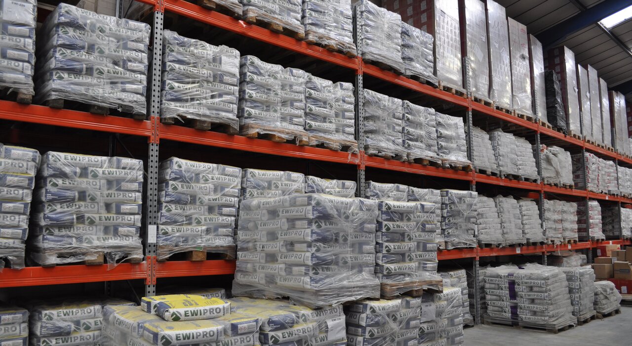 high-bay warehouse storage filled with palletised bags of EWI Pro products, showcasing stock availability and logistics capability of EWI Store – a company specialising in external wall insulation and render systems
