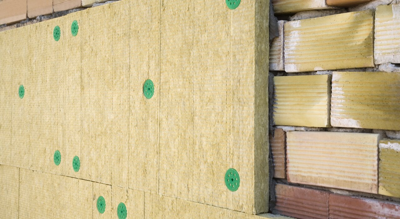 Mineral wool insulation boards mechanically fixed to a brick wall using green insulation fixings as part of an external wall insulation system