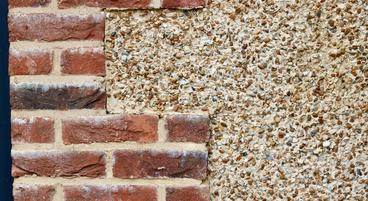 Close-up of a brick wall partially covered with pebble dash render, showing a transition between traditional brickwork and aggregate render finish commonly encountered during external wall insulation retrofits