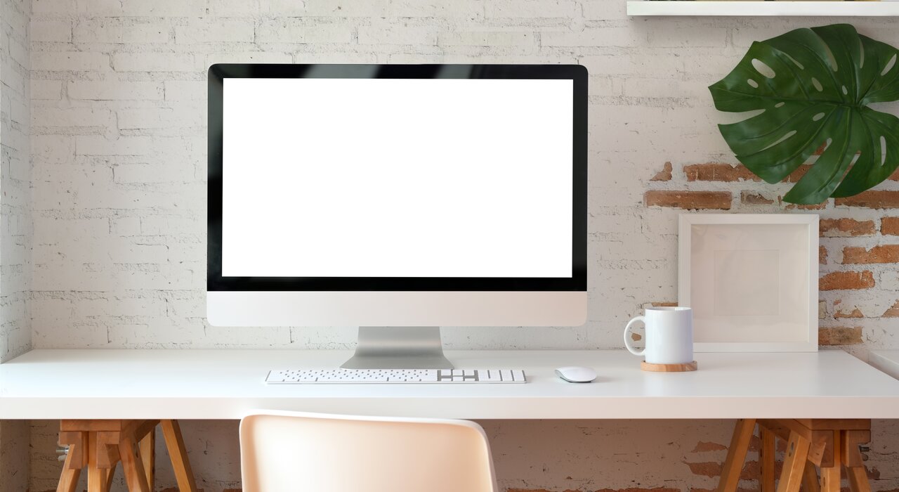 Minimalist desktop workspace with a blank computer screen in front of a white and exposed brick wall, suitable for using external wall insulation tools like material calculators or installer portals