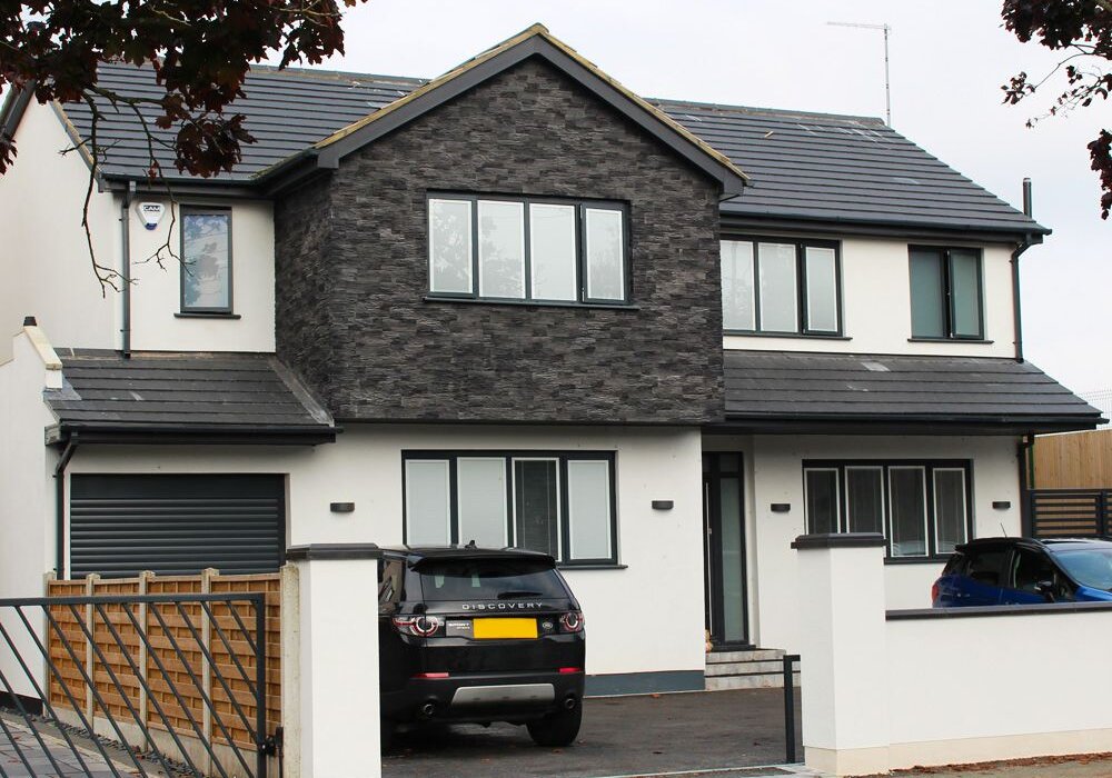 Modern detached house finished with crisp white render and dark stone cladding, showcasing a clean, contemporary look with external wall insulation for improved energy efficiency and curb appeal.