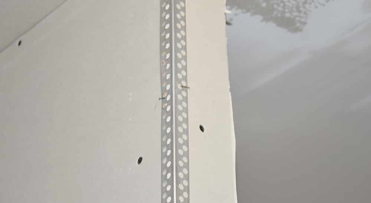 This image displays a drywall corner with a perforated metal corner bead installed. Corner beads like this are commonly used in both internal and external wall insulation systems to protect corners, provide clean finishes, and reinforce plaster or render application.