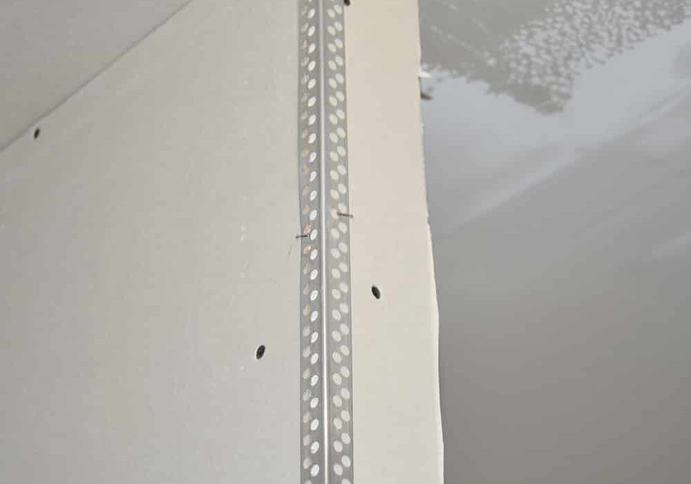 This image displays a drywall corner with a perforated metal corner bead installed. Corner beads like this are commonly used in both internal and external wall insulation systems to protect corners, provide clean finishes, and reinforce plaster or render application.