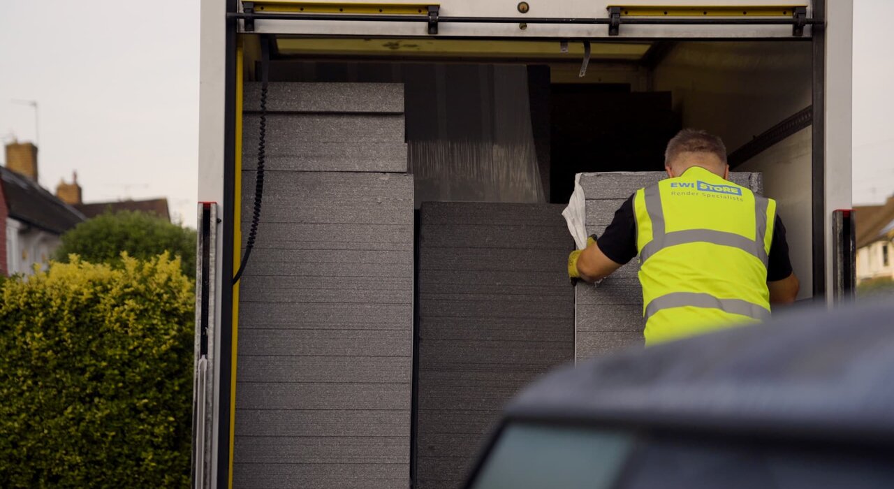 EWI Store employee unloading grey EPS insulation boards from a delivery van at a residential property. These boards are key components of external wall insulation systems, improving energy efficiency and reducing heat loss.
