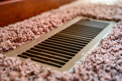 Close-up of a floor air vent surrounded by carpet, part of a home ventilation or heating system. Proper airflow like this, combined with external wall insulation and quality render systems from companies like EWI Store, supports healthier indoor environments and improved energy efficiency.
