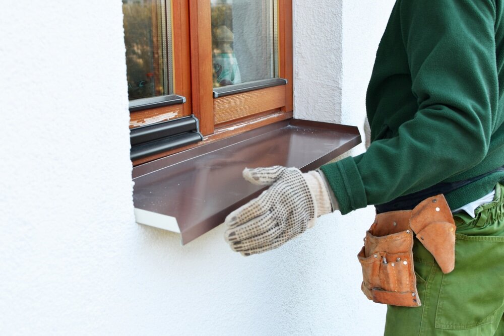 Installer fitting an external aluminium window sill beneath a timber-framed window, on a property finished with external wall insulation and render. EWI Store supplies full systems including sills, profiles, and insulation materials for professional, weather-resistant finishes.