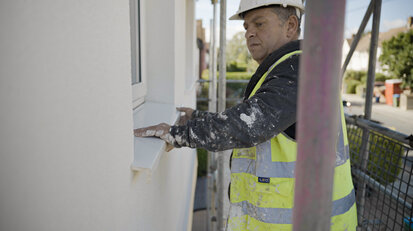 Construction worker installing a window sill detail on a freshly rendered façade with external wall insulation. Part of a professional EWI system application, supplied by EWI Store—experts in insulation and rendering solutions for energy-efficient homes.