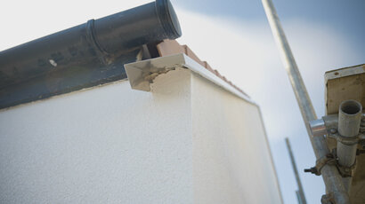 Close-up of a roof verge detail with metal flashing installed over a rendered gable wall finished with external wall insulation. The flashing helps protect the EWI system from water ingress, ensuring long-term durability—part of the complete systems available from EWI Store.