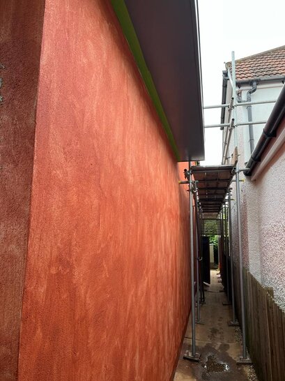 Freshly applied basecoat primer in a bold red-orange tone on an external wall, preparing the surface for the final render layer. This essential step improves adhesion and coverage for topcoat renders in external wall insulation systems—products available from EWI Store, specialists in EWI and rendering solutions.