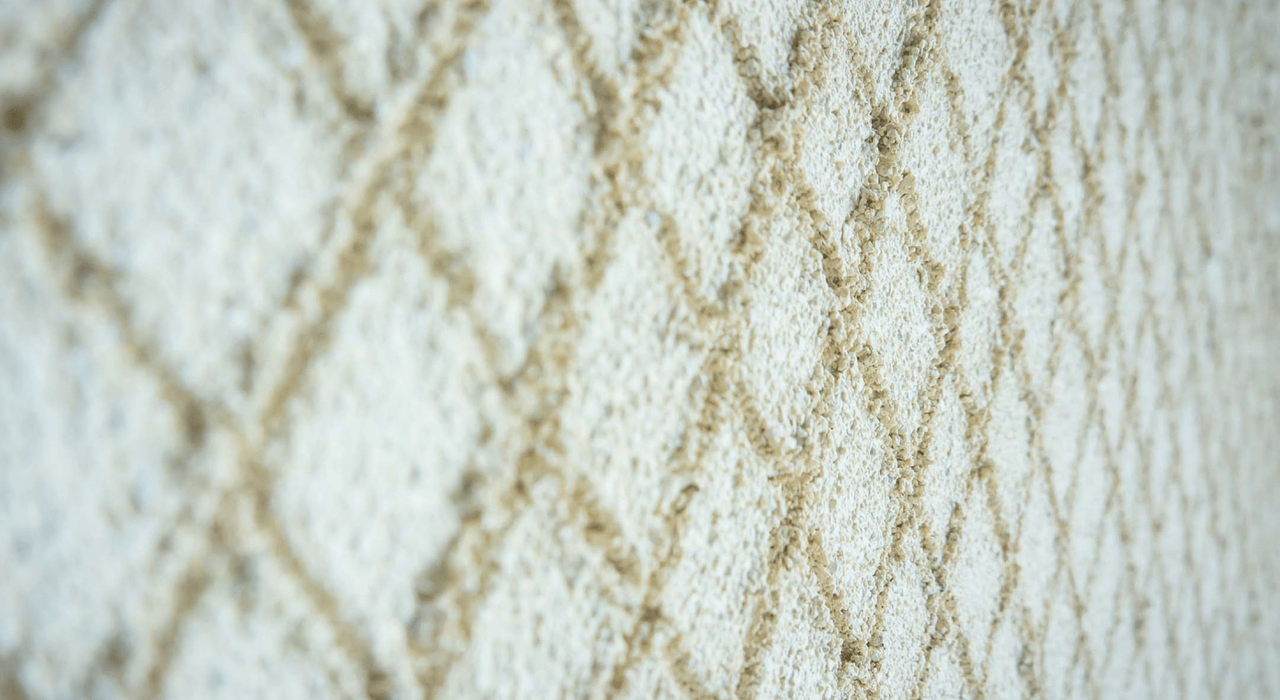 Close-up of a scratch render finish in a light beige tone with a distinctive diamond texture. This decorative render style is both durable and breathable, commonly used in external wall insulation systems. EWI Store supplies a full range of monocouche and silicone-based scratch renders for professional façade finishes.