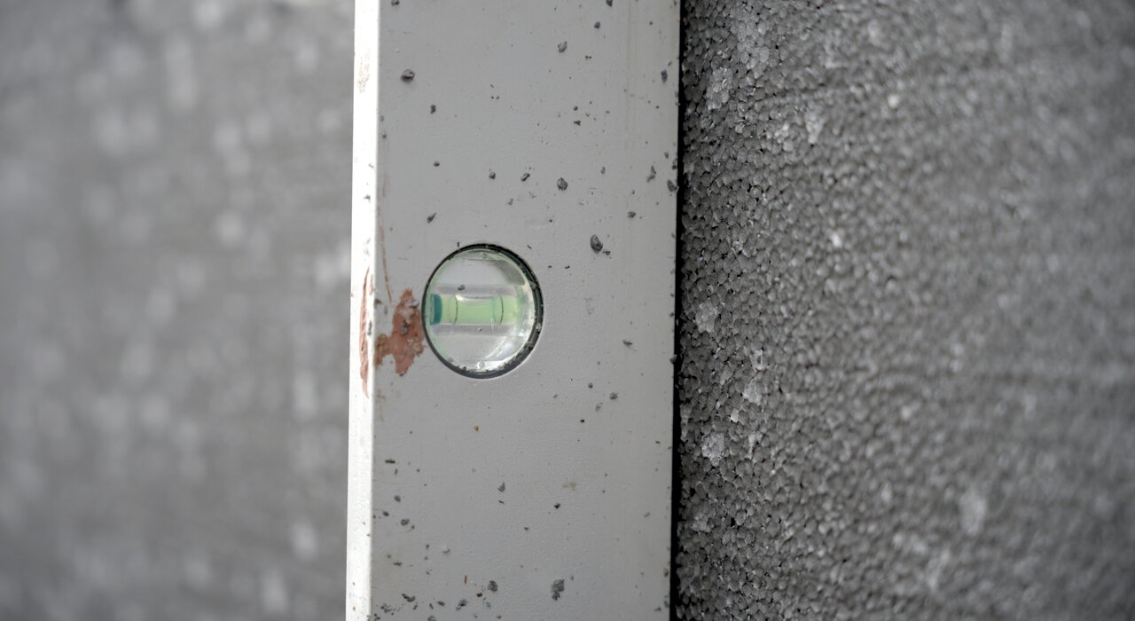 Close-up of a spirit level checking the alignment of grey EPS insulation boards during external wall insulation installation. Proper levelling ensures a smooth substrate for basecoat and render application. All tools and materials used in this process are available from EWI Store for professional and precise EWI systems.
