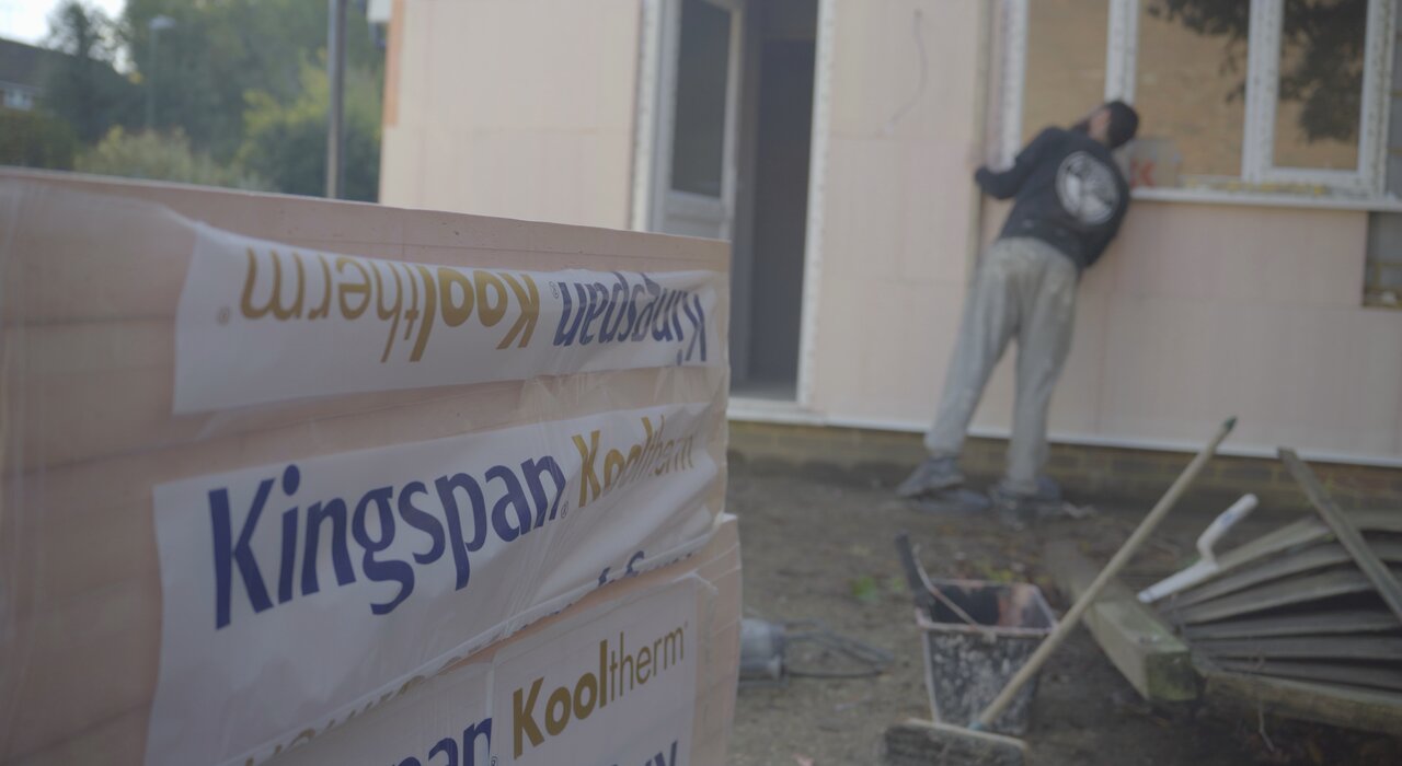 Close-up of Kingspan Kooltherm insulation boards on-site during an external wall insulation installation. In the background, an installer works on fitting the boards to the property façade. Kooltherm boards offer excellent thermal performance with minimal thickness, making them ideal for space-conscious EWI systems. Materials like these are available through EWI Store for high-efficiency retrofit and new-build projects.
