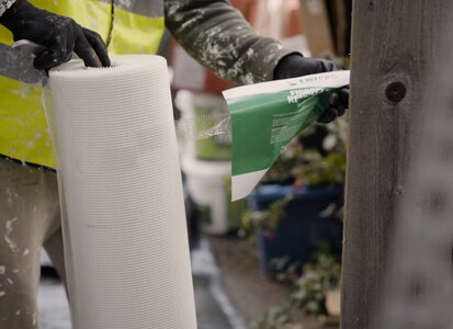 An installer holding a roll of fibreglass reinforcing mesh from EWI Pro. This mesh is embedded into the basecoat of an external wall insulation system to add strength and crack resistance before the final render is applied. EWI Store stocks a wide range of mesh types for different render systems.