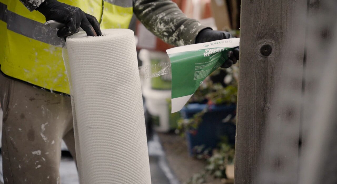 An installer holding a roll of fibreglass reinforcing mesh from EWI Pro. This mesh is embedded into the basecoat of an external wall insulation system to add strength and crack resistance before the final render is applied. EWI Store stocks a wide range of mesh types for different render systems.