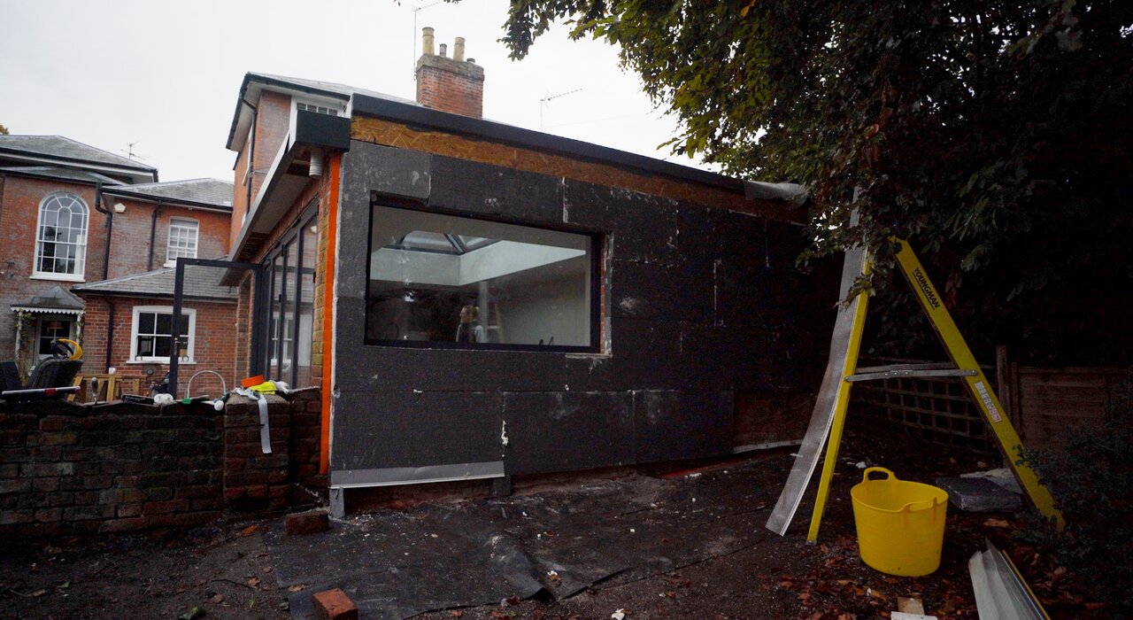 An external wall under construction, featuring dark grey EPS insulation boards installed on a single-storey extension. This phase shows the mechanical fixing stage before mesh and render layers are applied. Materials like these are part of complete EWI systems offered by EWI Store.