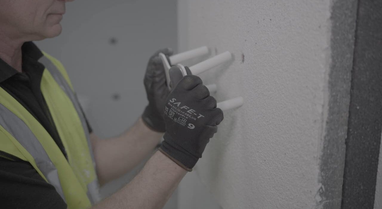 Close-up of an installer inserting thermal pin fixings through an insulation layer into a substrate wall. These mechanical fixings secure insulation boards to the external façade and prevent thermal bridging. Products like these are part of the EWI systems supplied by EWI Store.
