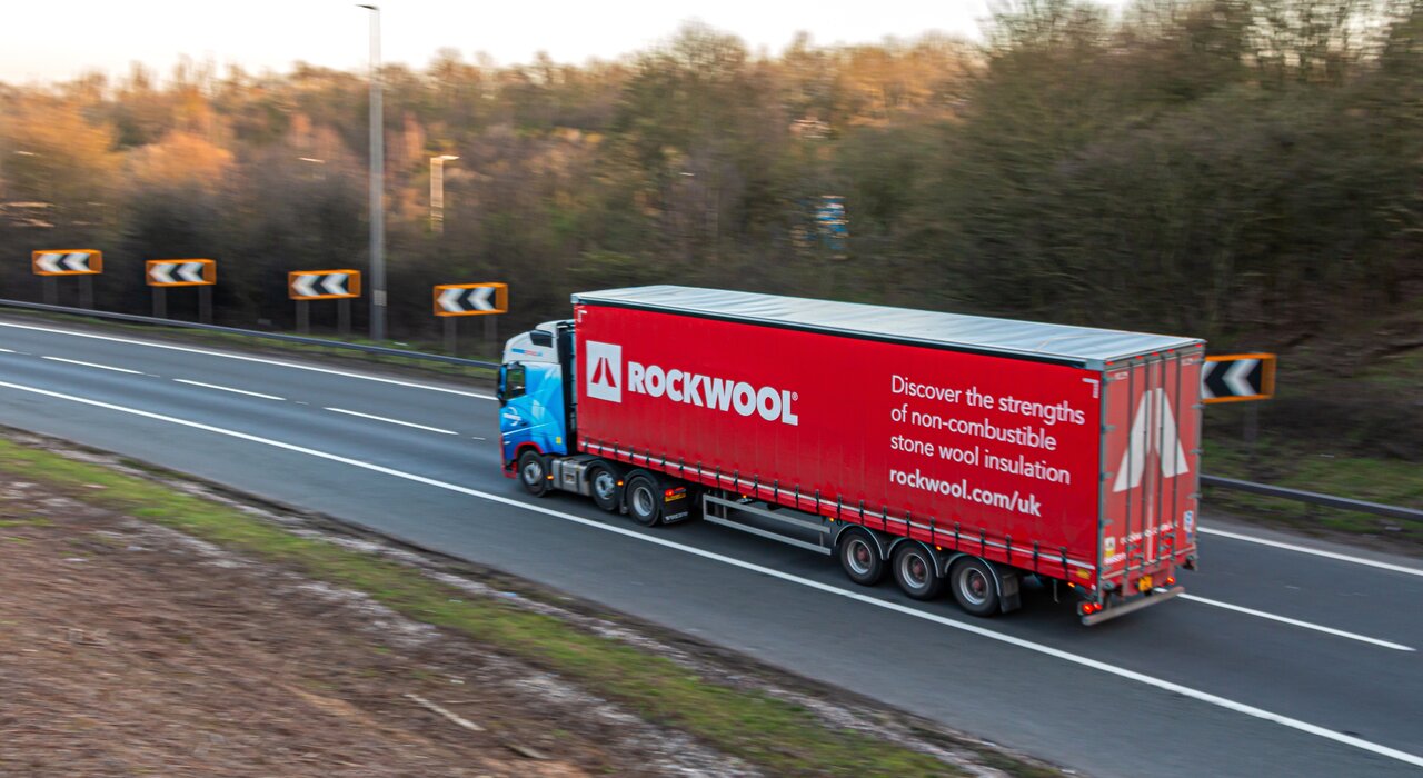 A Rockwool-branded lorry on the motorway delivering stone wool insulation. The message promotes its non-combustible, high-performance properties. Rockwool products are available through EWI Store and are ideal for fire-resistant, breathable, and thermally efficient wall systems.