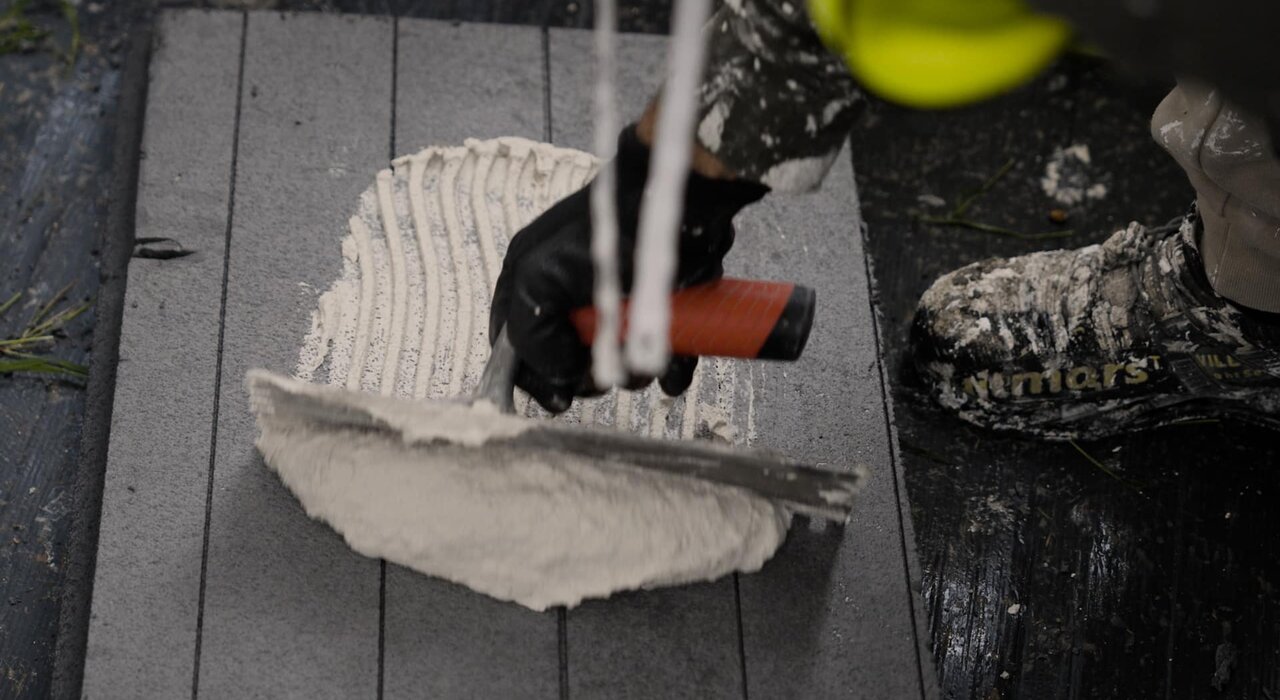 This image shows a worker applying adhesive to an insulation board as part of an external wall insulation system, using a high-quality notched trowel from **Regal & Barnes**, a trusted brand known for professional-grade tools in rendering and insulation work.