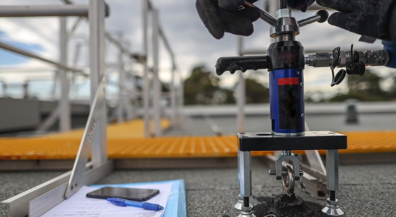 A close-up of a pull-out test being performed on a rooftop to assess the mechanical fixings of an external wall insulation system, with tools, gloves, and documentation visible to ensure compliance and structural integrity.