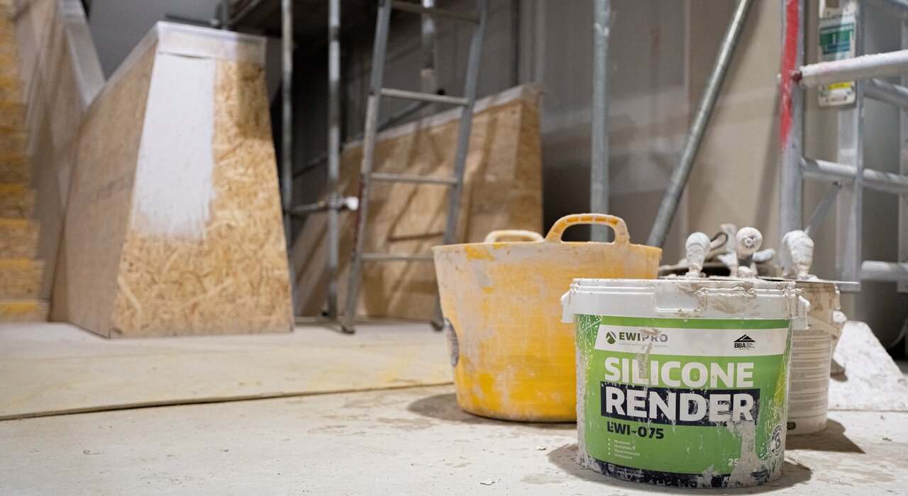 A tub of EWI Pro Silicone Render (EWI-075) sits in a construction area, highlighting its essential role in achieving a high-quality decorative finish for external wall insulation projects.