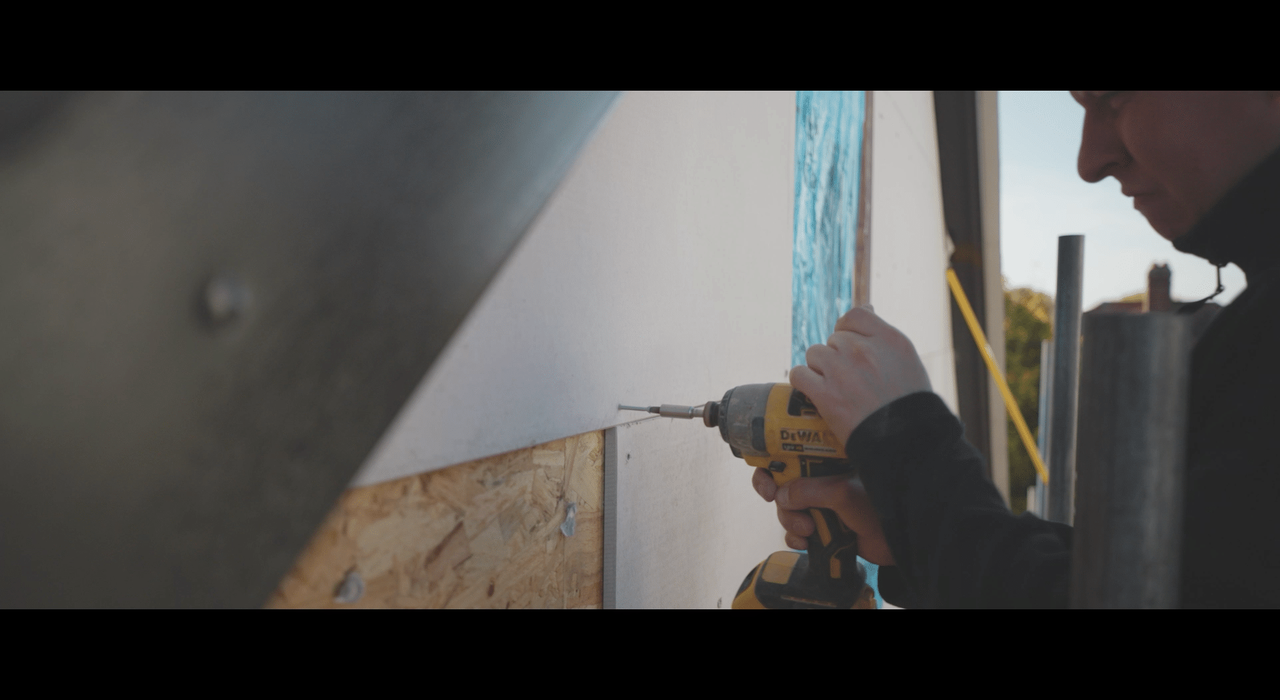 Worker using a DeWalt power drill to fasten insulation boards onto an external wall, demonstrating a key stage in the installation of external wall insulation systems.