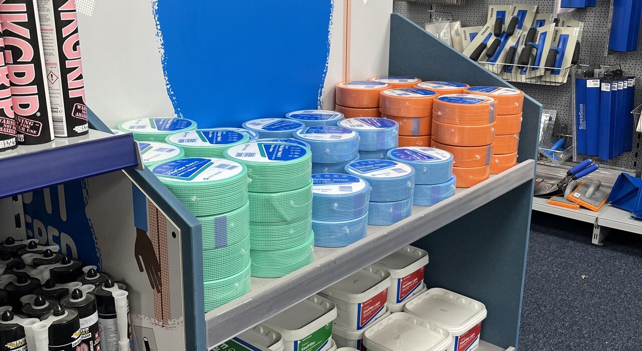 Display shelf located in the EWI Store shop featuring Gyproc products, including jointing tapes, filler tubs, and adhesive tubes, with a selection of decorating and plastering tools displayed on the wall behind.