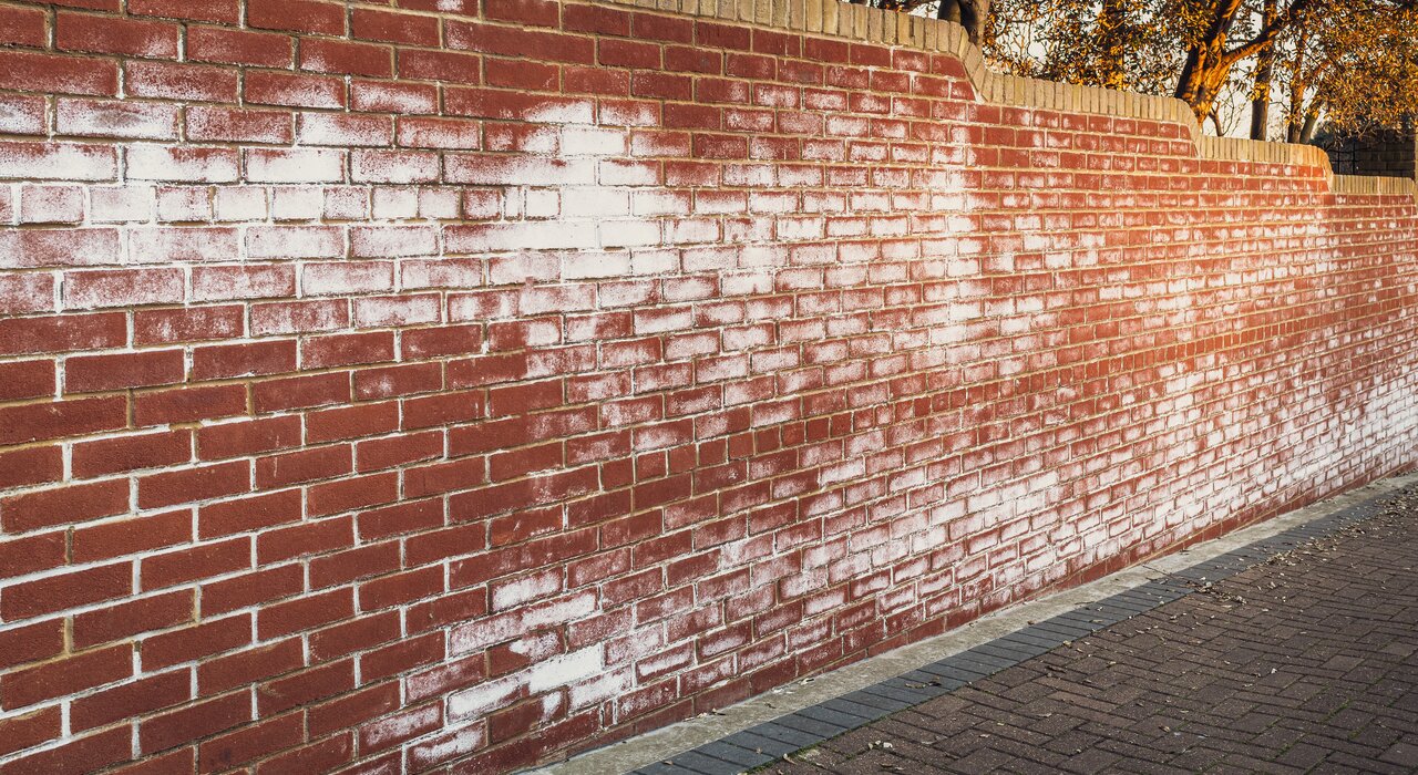 A red brick wall showing signs of efflorescence—white salt deposits on the surface—highlighting the importance of proper external wall insulation to prevent moisture ingress and related damage.