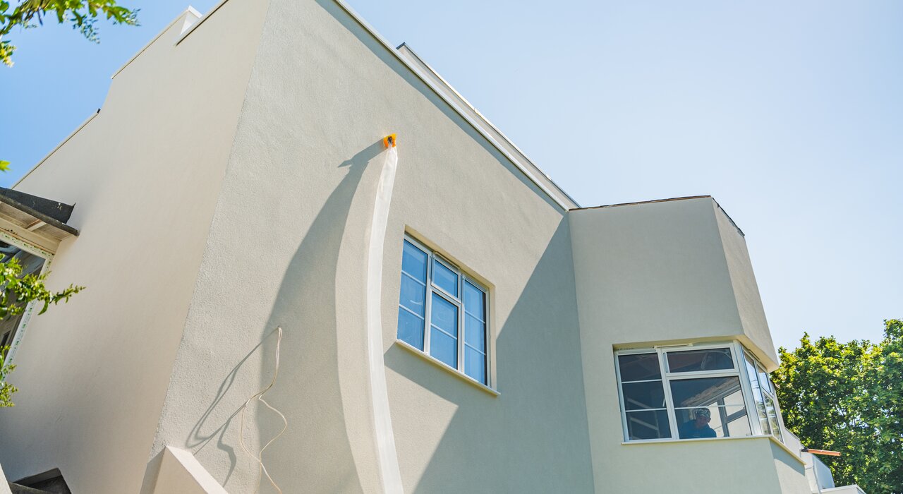 Exterior view of a modern, freshly rendered white building with clean lines and smooth walls, showcasing a newly applied render finish under a bright, clear sky. This type of render is commonly used for insulation and aesthetic improvements.
