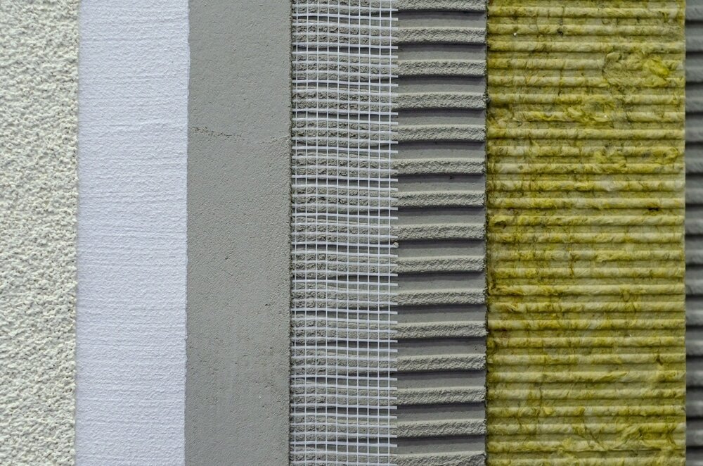 Cross-section of an external wall insulation system showing multiple layers including render, basecoat, mesh reinforcement, adhesive, and mineral wool insulation.