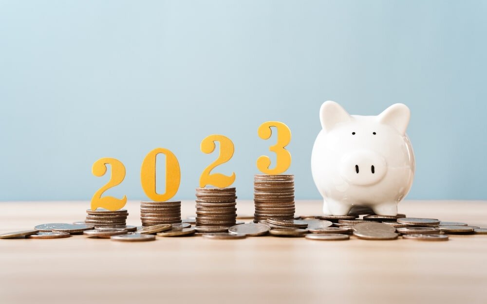 A white piggy bank sits beside stacks of coins, each topped with the numbers 2023, symbolising financial growth or savings in the year 2023.