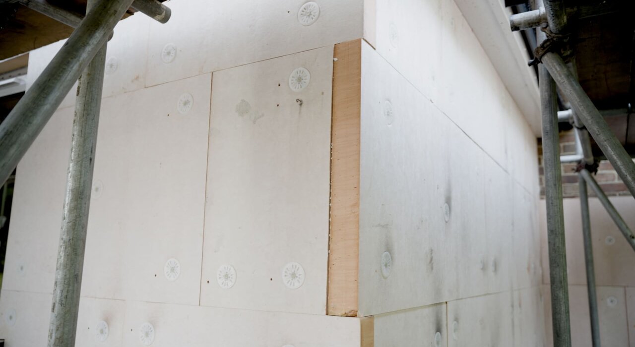 This image shows external wall insulation panels being installed on a building, which helps improve energy efficiency by reducing heat loss through walls.