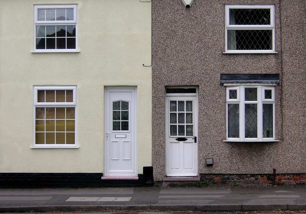 This photo shows two terraced houses with different finishes. The left house has a smooth painted finish, while the right one has roughcast or pebbledash, showing a clear visual and material contrast.