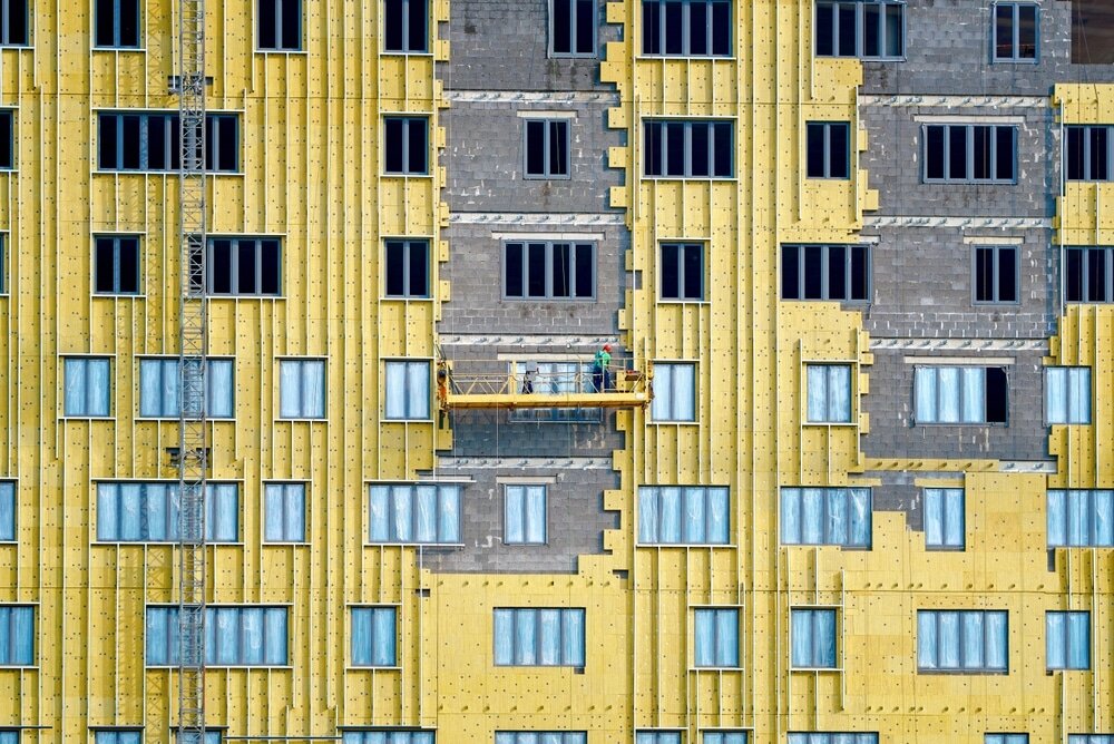 This image shows insulation boards being installed on the facade of a building. The yellow boards are part of the external wall insulation system, improving energy efficiency.