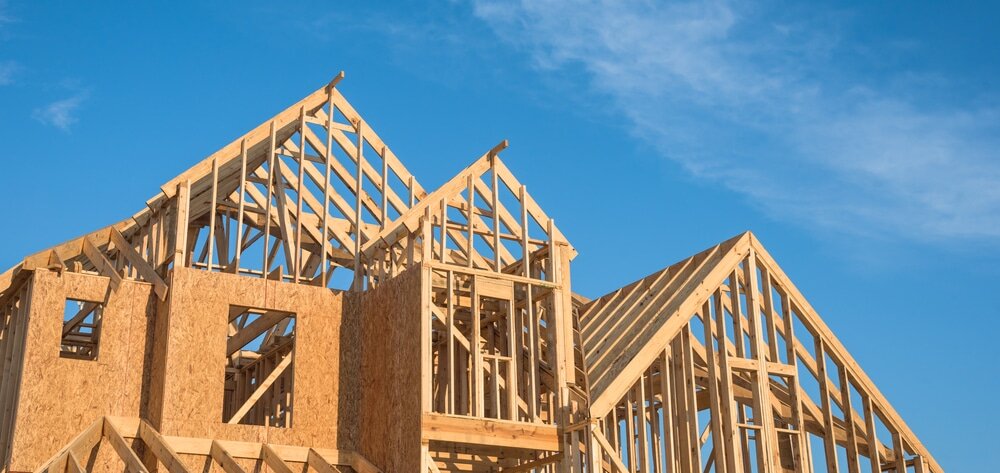Wooden house framework under construction against a clear sky.  Timber-framed buildings like this can benefit from external wall insulation to improve airtightness and reduce thermal bridging, especially when insulated externally before cladding is applied.