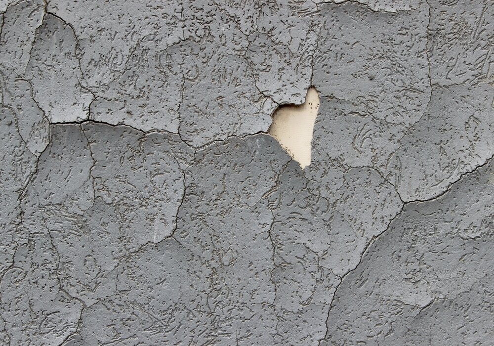 Close-up of a render façade with extensive cracking and peeling, revealing the underlying layer. This is often caused by poor adhesion, thermal stress, or lack of reinforcement mesh. EWI Store offers mesh, basecoats, and primers to help prevent such issues.