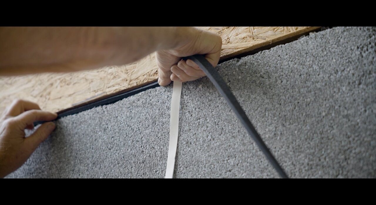 Close-up of a worker applying expanding foam tape between insulation boards and an OSB substrate. This air-tightening detail is crucial for sealing gaps and joints in EWI systems, improving airtightness and preventing thermal bridging.