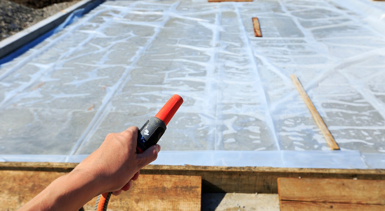 A worker spraying water onto a damp-proof membrane installed over a foundation slab. This step may be part of testing or curing preparation. Proper DPMs are essential for preventing rising damp in insulated buildings.