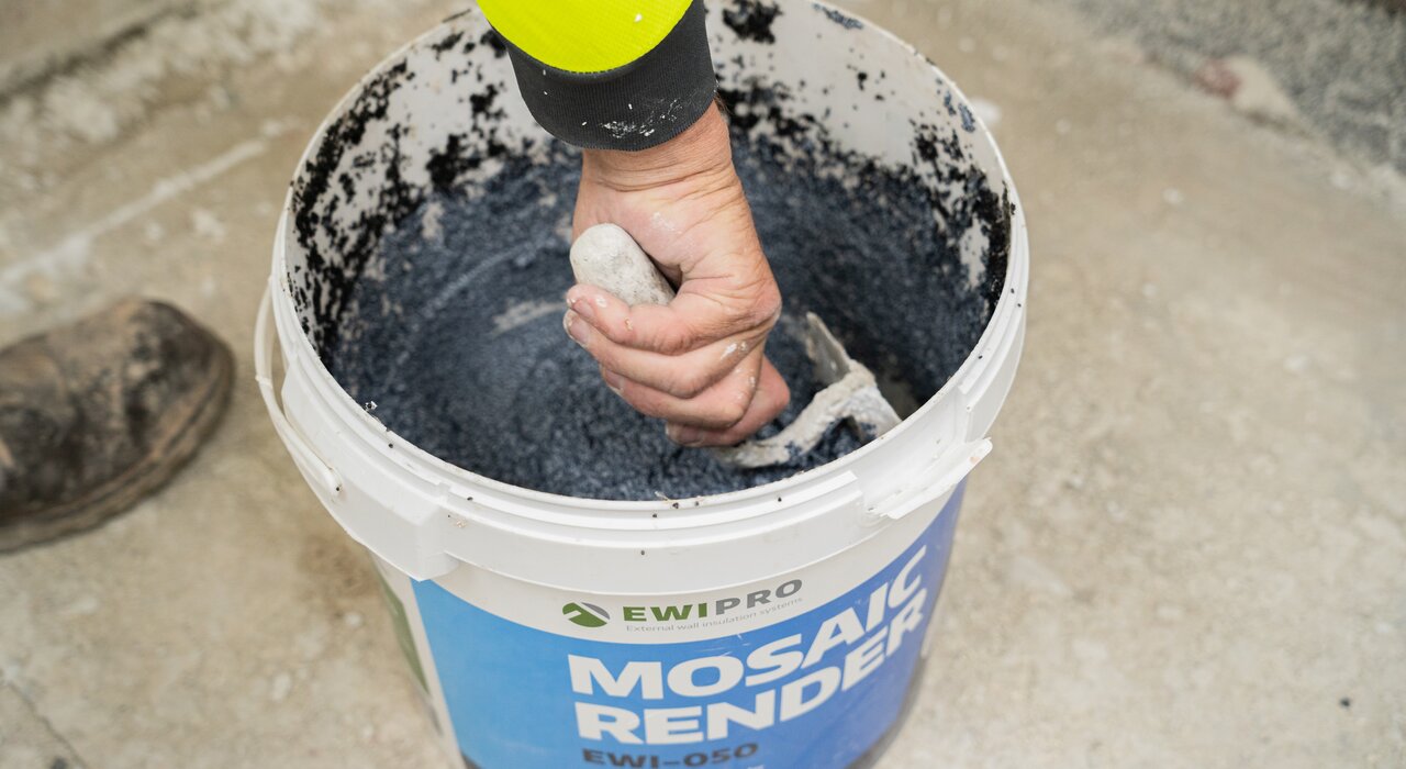 Close-up of a worker hand-mixing EWI Pro Mosaic Render (EWI-050) in a bucket. This decorative and durable render contains natural marble granules, making it ideal for use on plinths, columns, or areas prone to impact. Available from EWI Store, Mosaic Render offers a long-lasting, low-maintenance finish with a premium appearance.