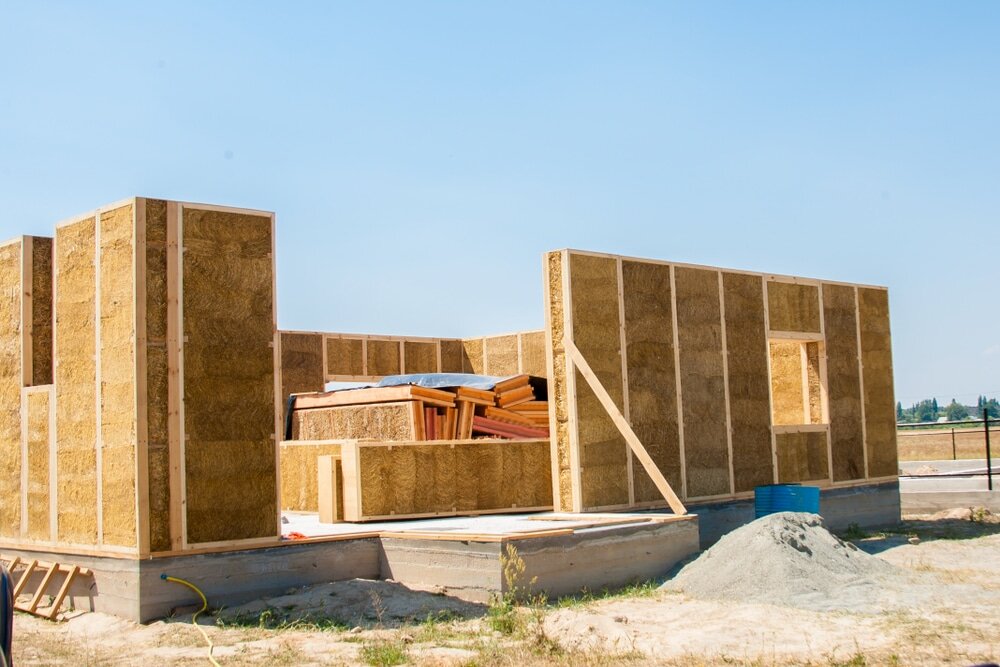 On-site photo of a timber frame building under construction, insulated with straw bale panels. This eco-friendly construction method provides excellent thermal performance with natural materials. EWI Store supports sustainable building—complement straw bale systems with breathable renders and insulation accessories from our product range.