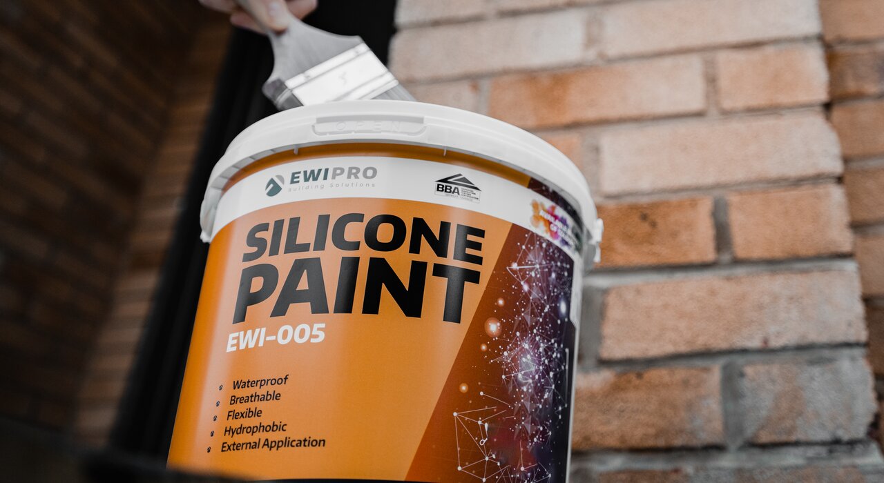 Close-up of a worker holding a tub of EWI Pro Silicone Paint (EWI-005) on-site, ready for exterior application. This waterproof, breathable, and flexible paint offers excellent hydrophobic protection, enhancing the longevity and appearance of rendered surfaces. Available at EWI Store, EWI Pro Silicone Paint is the perfect finishing touch for any external wall insulation project.