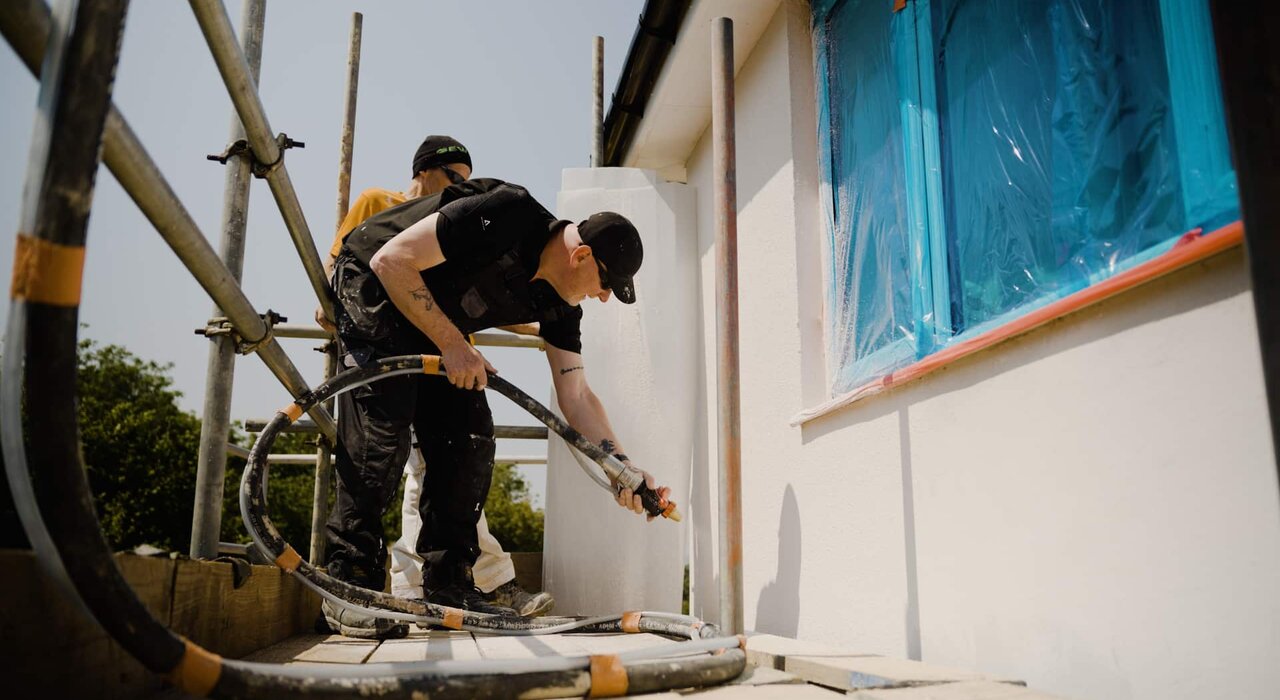Two applicators spraying render onto an external wall using a high-performance render spray machine. Surfaces have been prepped and masked for precision application. At EWI Store, we supply advanced spray equipment and full system solutions to support efficient, professional render installations at scale.
