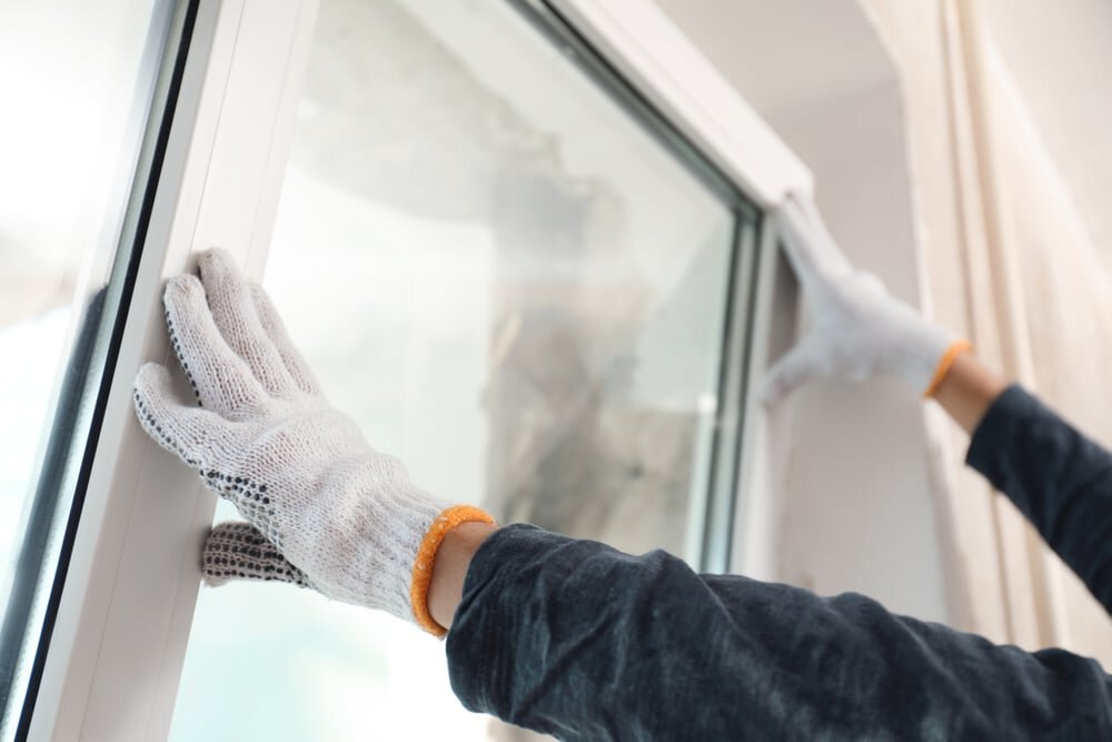 Close-up of a window installation in progress, with gloved hands carefully positioning the frame. EWI Store supplies all necessary components for EWI systems, including insulation-compatible window profiles and beading to ensure seamless integration and airtight results.