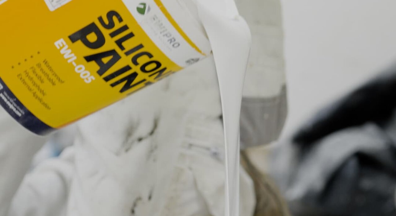 Close-up of a worker pouring EWI Pro Silicone Paint (EWI-005) into a roller tray. This flexible and breathable topcoat is designed for exterior application, offering hydrophobic protection and long-lasting colour retention. Available from EWI Store, Silicone Paint enhances façade durability while providing a clean, professional finish.