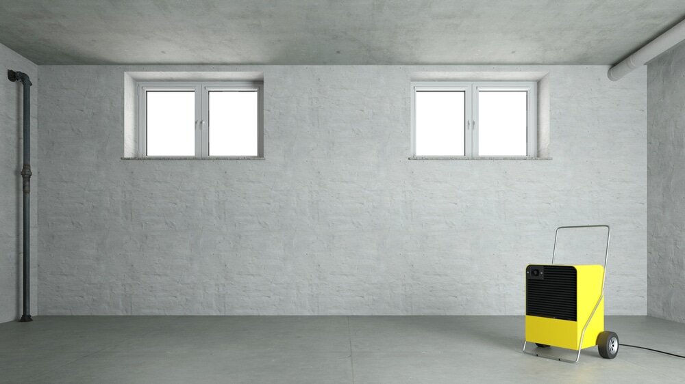 Wide shot of a dehumidifier operating in a basement with concrete floors and white walls. Controlling humidity is key when preparing walls for external wall insulation. EWI Store offers dehumidifiers and accessories to help maintain ideal conditions for adhesion and curing of basecoats, primers and renders.