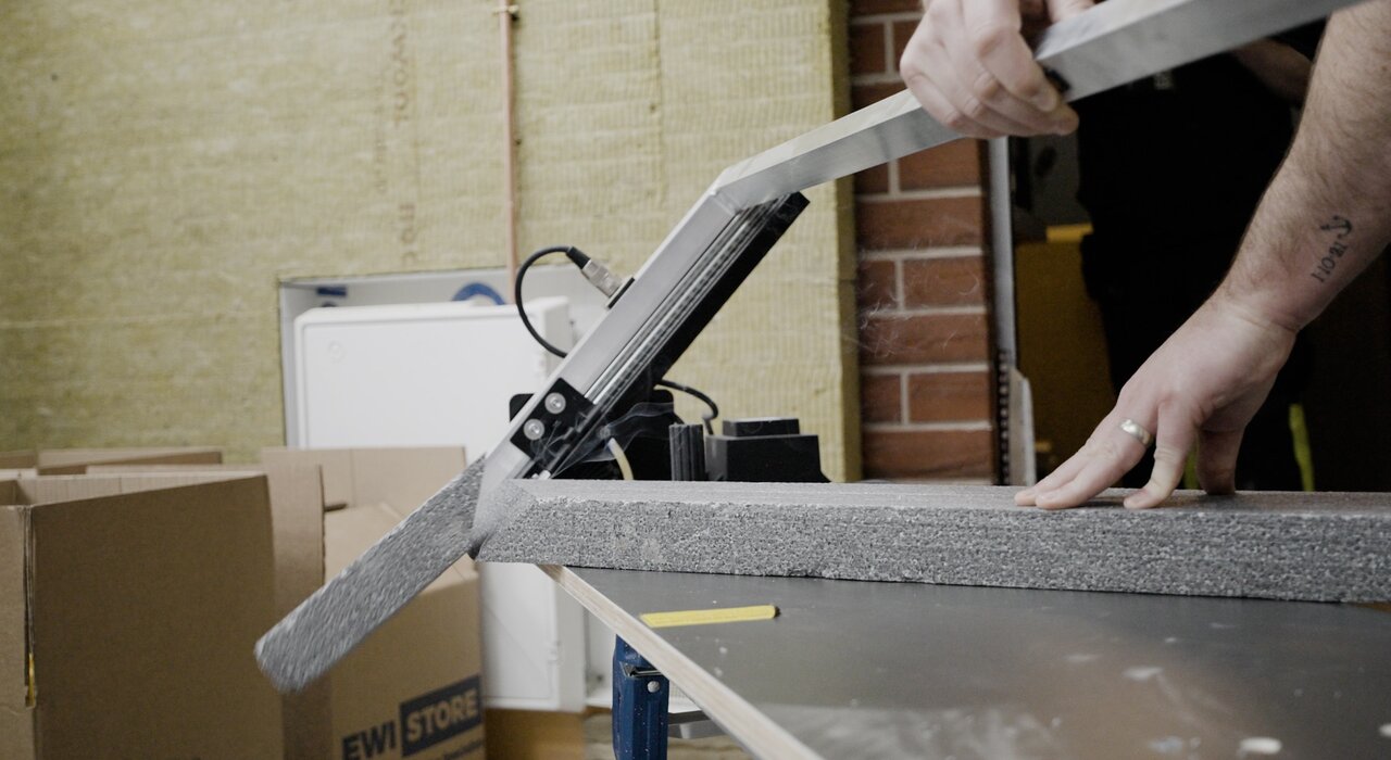 Close-up of a worker using a hot wire cutter to trim EPS insulation board. Precision cutting is essential for effective installation. Available from EWI Store, our hot wire cutters ensure clean, accurate cuts—minimising gaps, reducing thermal bridging, and improving insulation performance.