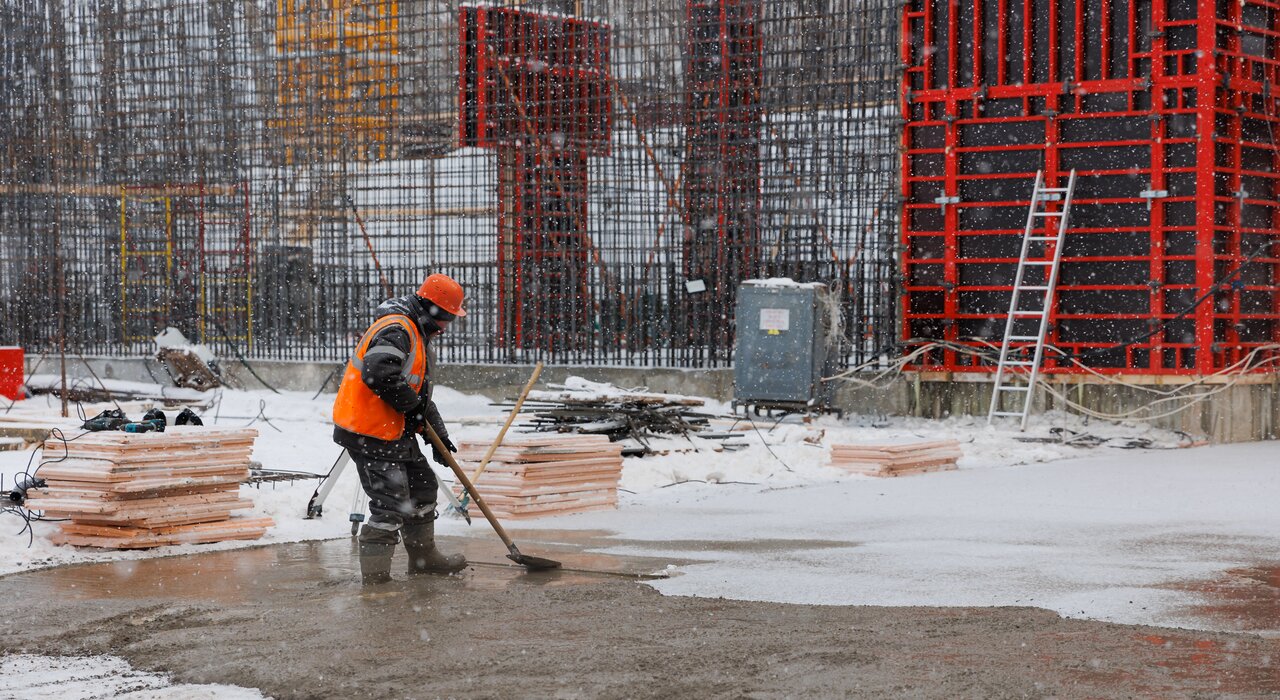 A worker spreads material on a concrete slab during snowfall on a construction site. Cold weather working demands high-performance materials. EWI Store provides winter-grade adhesives, renders and additives to ensure insulation systems can be installed safely and effectively in sub-zero temperatures.