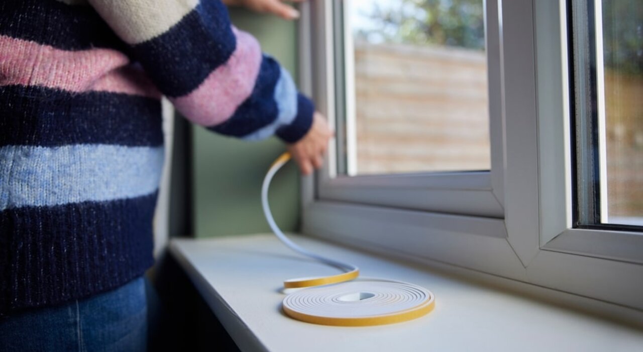 Close-up of a person applying window insulation tape. Properly sealing around window frames helps prevent drafts and reduces heat loss. Available from EWI Store, insulation tapes are an easy, cost-effective way to improve energy efficiency and enhance indoor comfort.