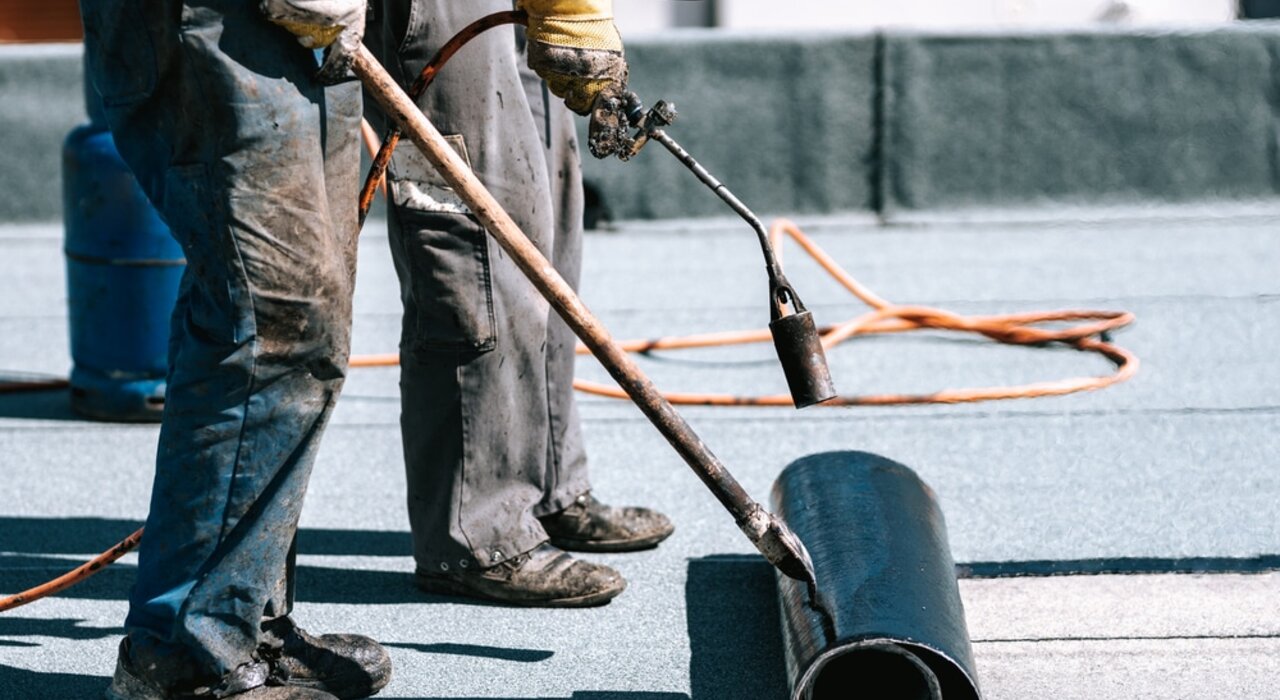 Workers installing torch-on bitumen membrane for flat roof waterproofing. This durable roofing solution protects against leaks and weather damage. EWI Store supplies high-performance membranes and tools for flat roof applications.