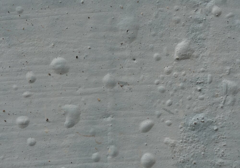 Close-up of render with signs of bubbling caused by trapped moisture or improper curing. Prevent rendering issues with high-quality breathable basecoats and primers from EWI Store, ensuring a durable and flawless finish.